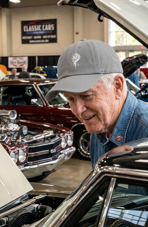Man wearing a gray Grit With Faith embroidered compass dad hat at an indoor classic car show